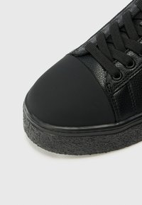Adidași negri cu un corp din piele texturată, vârf din cauciuc și o talpă groasă, texturată. Designul include șireturi și orificii pentru șireturi negre.