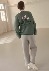 Sudadera verde con estrellas rosas y el texto "Los Angeles DANCE PALACE", combinada con pantalones de chándal grises y zapatillas blancas.