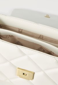 Λευκός καπιτονέ δερμάτινος φάκελος με χρυσό κούμπωμα και μπεζ εσωτερική επένδυση με τυπωμένο σχέδιο λογοτύπου.