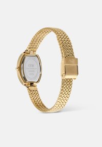 Reloj de pulsera en tono dorado con una correa de malla tejido, esfera ovalada y cierre de gancho. La parte trasera presenta el logo de la marca y detalles del producto.