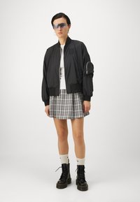 Black bomber jacket with front zip and side pocket, white t-shirt, gray plaid pleated skirt, black lace-up boots, and white socks.