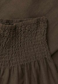 Bruine stof met een geraffineerde smockingdetail op de taille. Zachte textuur, met een uitlopende vorm en een subtiele glans. Geen duidelijke patronen of hardware zichtbaar.