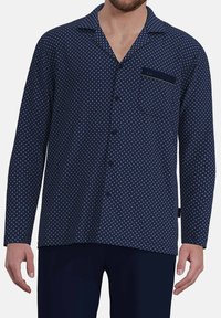 Button-up shirt in navy fabric featuring a geometric pattern in gold. Long sleeves, collar, and a chest pocket with a label.