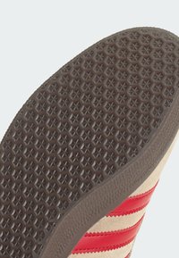 Σόλα αθλητικού παπουτσιού με καφέ ελαστική επιφάνεια που διαθέτει μοτίβο αστεριών; η πλευρά δείχνει μπέζ σουέντ και κόκκινες δερμάτινες ρίγες.