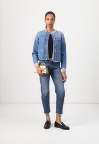 Veste en denim bleu moyen, design court avec deux poches avant et fermeture à boutons. Associée à un jean droit et un petit sac à main beige.