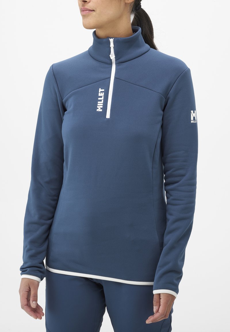 Pull en polaire bleu marine avec col haut, fermeture éclair blanche, et logo sur la poitrine et la manche. Texture lisse avec un liseré blanc contrastant.