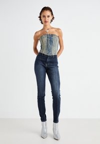 Denim korsetski top s izfrčenim rubom, u kombinaciji s tamnoplavim uskim trapericama koje imaju prednji šav, te s blještavim srebrnim čizmama do gležnja.