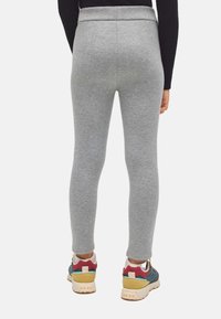 Mallas grises hechas de un tejido elástico con un diseño ajustado. Combinadas con zapatillas multicolores que tienen una suela texturizada y acentos superpuestos.