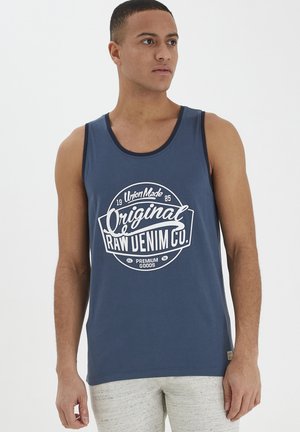 Tamno plavi majica bez rukava izrađena od pamuka, s bijelim grafičkim dizajnom koji sadrži tekst "Original Raw Denim Co" u retro stilu. Glatka tekstura.