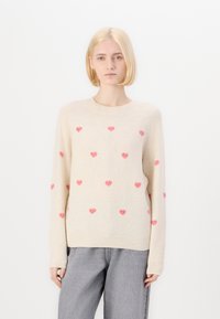 Pull léger beige en tissu doux, orné de motifs de cœurs roses éparpillés, avec un col rond et des poignets et un ourlet côtelés.