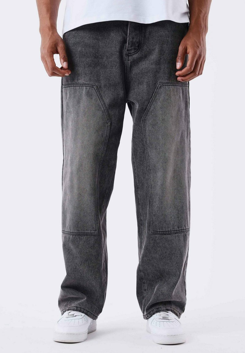 Pantaloni in denim grigio scuro con una vestibilità rilassata, dotati di tasche a toppa e cuciture in vista. Indossati con sneakers bianche.