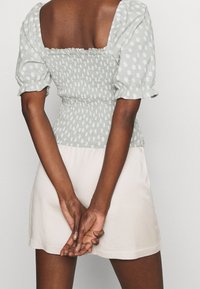 Blusa verde claro con puntos, con mangas abullonadas y un diseño fruncido. Combinada con una falda de color crema hasta la rodilla.