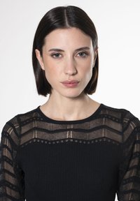 Schwarzes langärmliges Oberteil mit geripptem unteren Abschnitt und transparenter Spitze im oberen Bereich, die horizontale Streifen und komplizierte Muster aufweist.