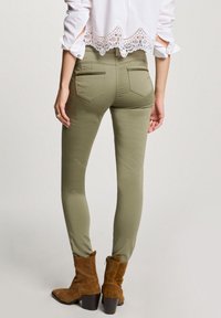 Olivově zelené skinny džíny se zadními kapsami, texturovaná tkanina a krátký bílý top s krajkovým lemem. Hnědé semišové kotníkové boty.