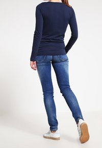 Marinblå långärmad skjorta kombinerad med slim fit blå jeans och lätta skor. Skjortan har en rund halsringning; jeansen har en klassisk femfickdesign.