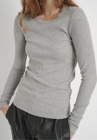 Hellgraues, langärmliges, geripptes Shirt mit rundem Ausschnitt und figurbetontem Schnitt. Kombiniert mit schwarzen Lederhosen.