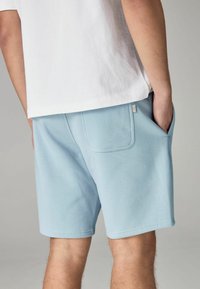 Shorts in cotone azzurro chiaro con tasca laterale, vestibilità rilassata e superficie liscia, abbinati a una maglietta bianca.
