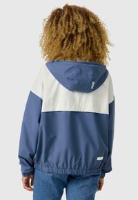 Veste à capuche colorée avec un design bleu marine et blanc, des poignets élastiques et une coupe décontractée. Texture de tissu lisse.