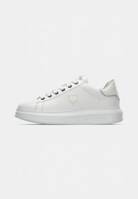 Baskets blanches en cuir à profil bas avec semelle épaisse, lacets blancs et logo embossé sur le côté et la semelle, sur fond clair uni.