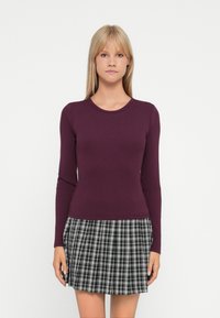 Burgundy long-sleeve ribbed top paired with a black and white plaid pleated skirt. Smooth texture and fitted silhouette.