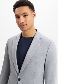 Hellgraue Anzugjacke mit texturiertem, kariertem Muster, Ein-Knopf-Verschluss, Reverskragen und einer Brusttasche über einem marineblauen Hemd.