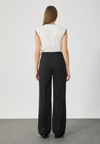 Fehér ujjatlan felső fekete díszítéssel, magas derekú fekete bővebb nadrággal párosítva. Simító anyag minimális részletezéssel.