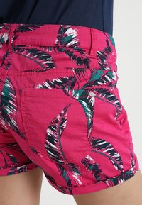 Pink shorts featuring a palm leaf pattern in green and white. Constructed from lightweight fabric, with belt loops and pockets.