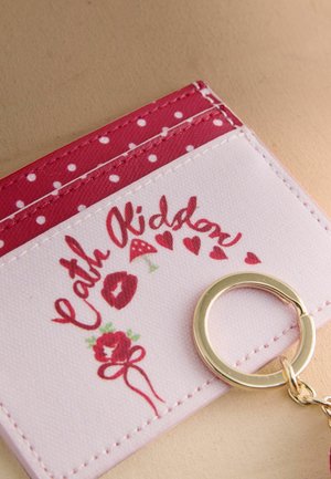 Keychain wallet in white and red with polka dots. Features a floral design, text, and a gold-colored metal keyring attached.