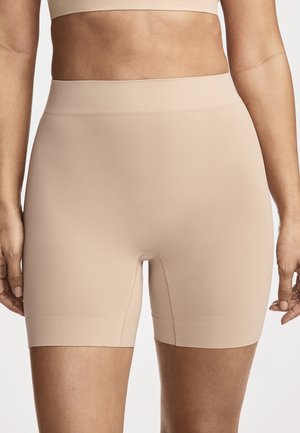 Woman wearing beige high-waist seamless compression shorts and matching sports bra, standing with arms relaxed at sides.