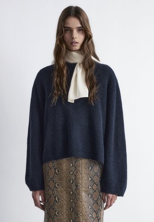 Navy oversized sweater with long sleeves, made of soft material, paired with a beige scarf and a brown snake-patterned skirt.