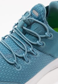 Modré sportovní boty vyrobené z textilního materiálu, s texturovaným svrškem, elastickým šněrováním a bílou podrážkou se zeleným vnitřkem.