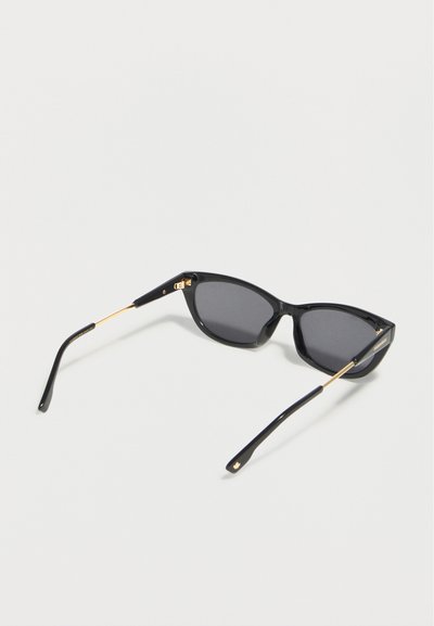 Μαύρα γυαλιά ηλίου με σκελετό cat-eye, χρυσούς βραχίονες και σκούρα φακούς σε λευκό φόντο.