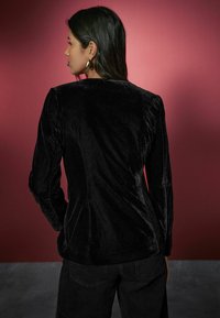 Black velvet long-sleeve top with a fitted silhouette and smooth texture, featuring a rounded neckline and subtle shoulder seams.