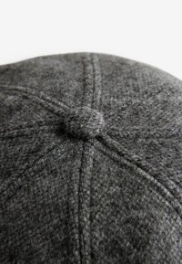 Grå ullmössa med rund form, prydd med en knuten knopp på toppen och synliga sömmönster. Texturerat, varmt material.