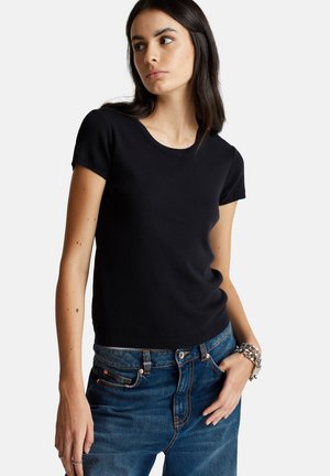 Haut tricot noir à manches courtes avec un col rond, présentant une texture lisse et un design ajusté, associé à un jean taille haute bleu.