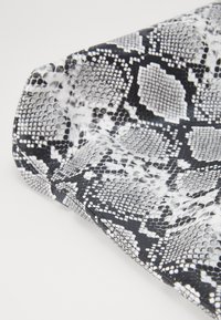Black and white faux snake skin pattern with textured scales. Smooth surface with a slight sheen, showcasing a folded edge.