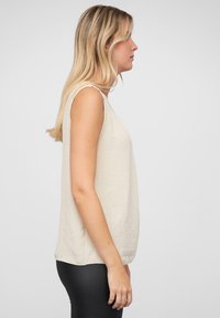 Hellbeige ärmelloses Oberteil mit strukturiertem Finish, lässiger Passform und abgerundetem Saum, kombiniert mit schwarzen Leggings. Seitenansicht gezeigt.