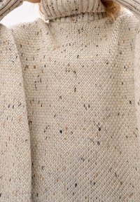 Mysig stickad tröja i krämfärg med prickiga detaljer. Har en hög, ribbad krage och vida ärmar, vilket framhäver den texturerade tyget.