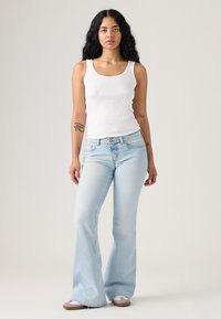 Hellblaue Jeans mit ausgestelltem Bein und mittlerer Taille, kombiniert mit einem weißen, gerippten Tanktop. Glatter Stoff und dezente Verwaschungseffekte.