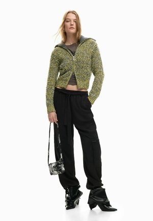 Knit cardigan in green and yellow with a hood, paired with black cargo pants and black heeled boots, featuring a small patterned bag.
