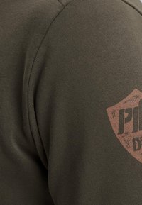 Olive zelená bavlnená mikina s okrúhlym výstrihom, s textúrovanou tkaninou a vyblednutým oranžovým logom potlačeným na pravej rukáve.
