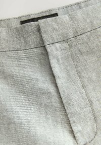 Šedá denimová látka s jemným vzorem rybí kosti, s propracovaným pasem a detailem vrchního prošití, úhlová klopa kapsy.