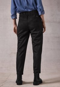 Sorte slim-fit bukser med en blød tekstur, elastisk talje og to baglommer. Sammen med ankelhøje sorte støvler.