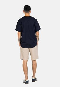 Camiseta de algodón de color azul marino con mangas cortas, combinada con pantalones cortos de textura beige y zapatos a rayas en blanco y negro.