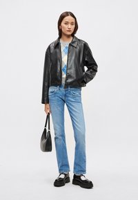 Čierna kožená skrátená bunda, sivý sveter s modrým vzorom argyle, svetlomodré džínsy, čierna kabelka, robustné čierne topánky.