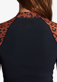 Rash guard noir avec des manches en imprimé léopard marron, présentant un col brodé et le logo embossé à l'arrière, fabriqué en matériau extensible.