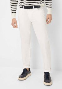 Witte katoenen broeken met een slim fit, voorzien van opgerolde boorden en een zwarte gevlochten riem. Gekoesterd met marineblauwe sneakers met een crèmekleurige zool.