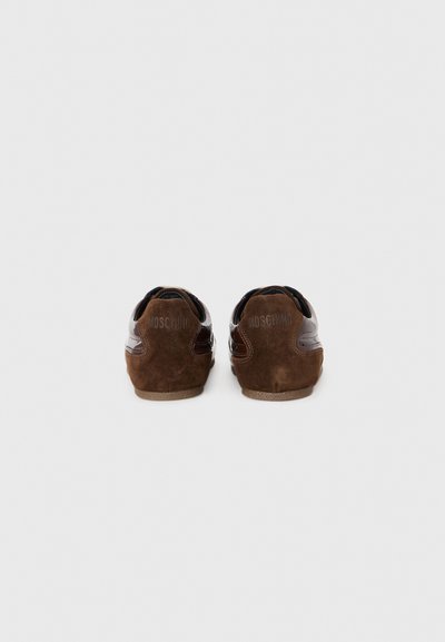 Bruna mockasiner i mocka med glansiga läderdetaljer, med en rund form och texturerade gummisulor. "Moschino"-logotypen präglad på baksidan.