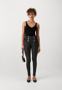 Débardeur noir à côtes associé à un pantalon noir taille haute avec des accents de boutons argentés et un design ajusté et élégant.