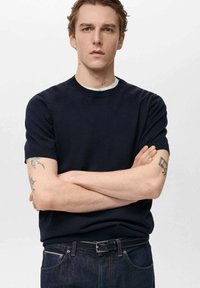 Námořnická modrá triko s krátkým rukávem a kulatým výstřihem, vyrobené z měkké látky, s kontrastním bílým vnitřním límečkem, nošené s tmavými džíny.